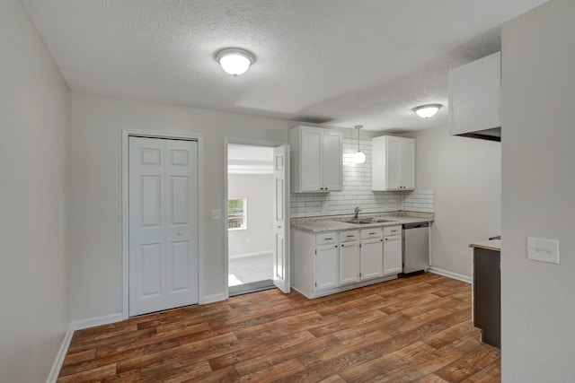 kitchen with pendant lighting, stainless steel dishwasher, white cabinets, hardwood / wood-style flooring, and decorative backsplash