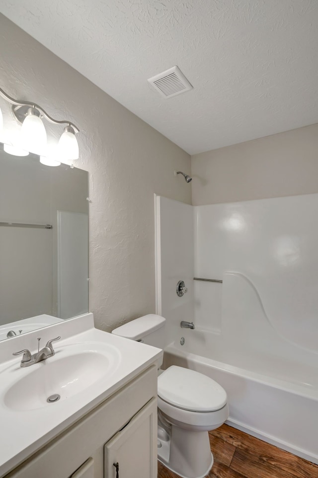 full bathroom featuring hardwood / wood-style flooring, toilet, shower / bathtub combination, vanity, and a textured ceiling