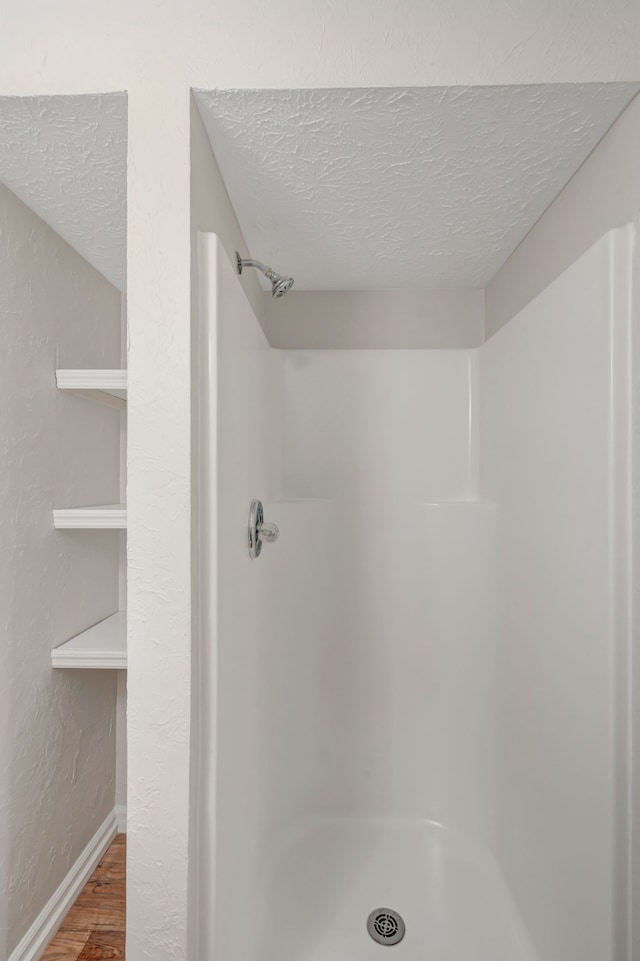 bathroom with hardwood / wood-style floors, walk in shower, and a textured ceiling