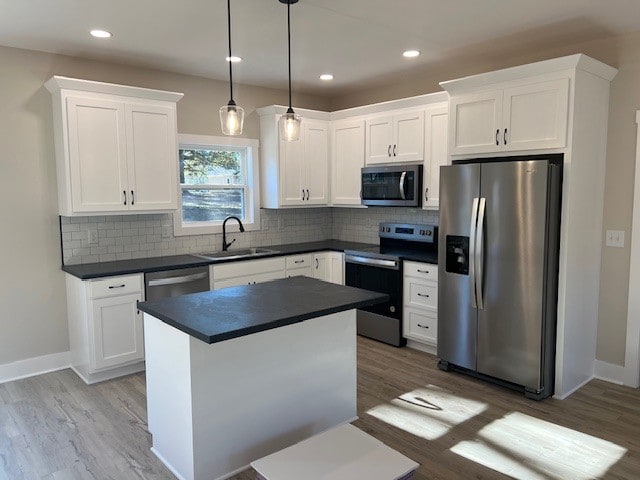 kitchen with appliances with stainless steel finishes, sink, pendant lighting, wood-type flooring, and white cabinetry