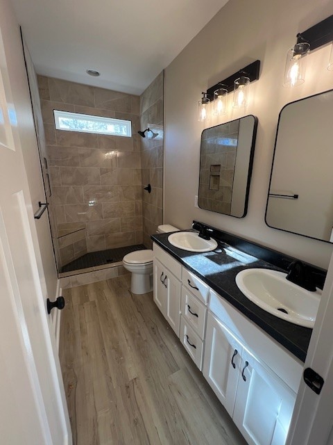 bathroom with hardwood / wood-style floors, vanity, toilet, and tiled shower