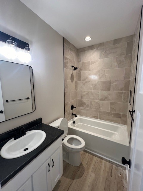 full bathroom with hardwood / wood-style floors, vanity, toilet, and tiled shower / bath