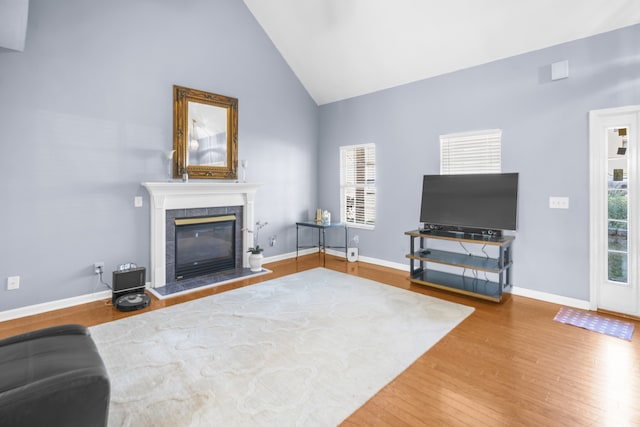 living room with hardwood / wood-style flooring, high vaulted ceiling, and a tiled fireplace