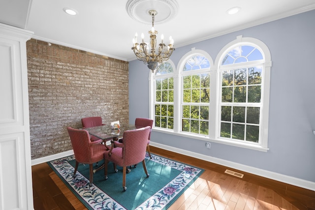 dining space featuring crown molding, hardwood / wood-style flooring, a chandelier, and brick wall