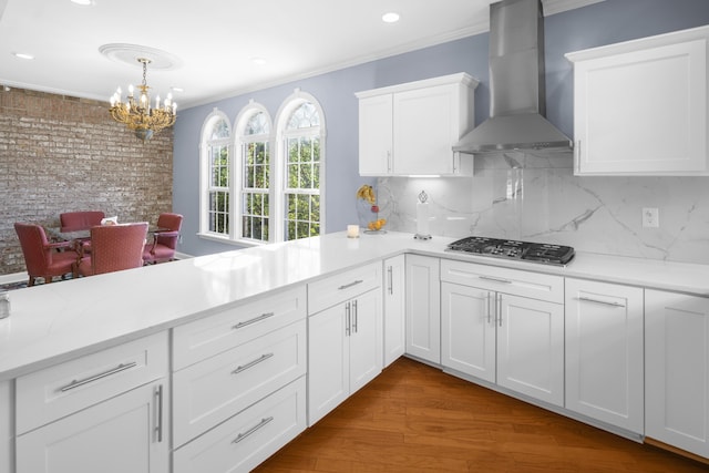 kitchen featuring tasteful backsplash, white cabinetry, wood-type flooring, crown molding, and wall chimney exhaust hood