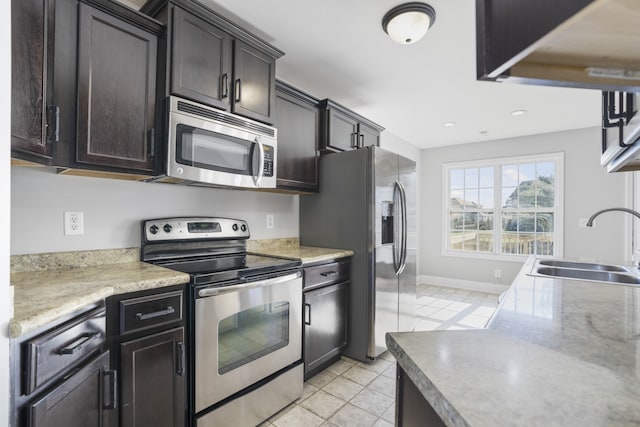 kitchen featuring stainless steel appliances, dark brown cabinetry, sink, and light tile patterned flooring