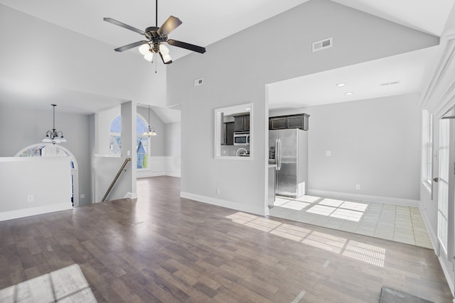 unfurnished living room featuring high vaulted ceiling, dark hardwood / wood-style flooring, and ceiling fan with notable chandelier