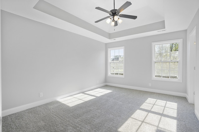 carpeted empty room with ceiling fan and a raised ceiling