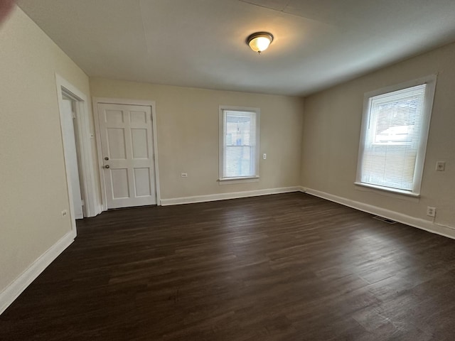 spare room featuring visible vents, baseboards, and dark wood finished floors