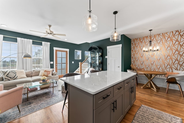 kitchen with light stone counters, decorative light fixtures, a breakfast bar area, ceiling fan with notable chandelier, and light wood-type flooring