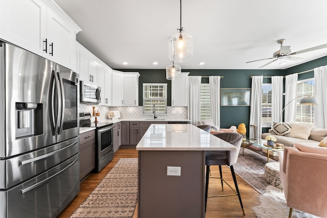 kitchen with white cabinetry, hanging light fixtures, stainless steel appliances, gray cabinets, and a breakfast bar