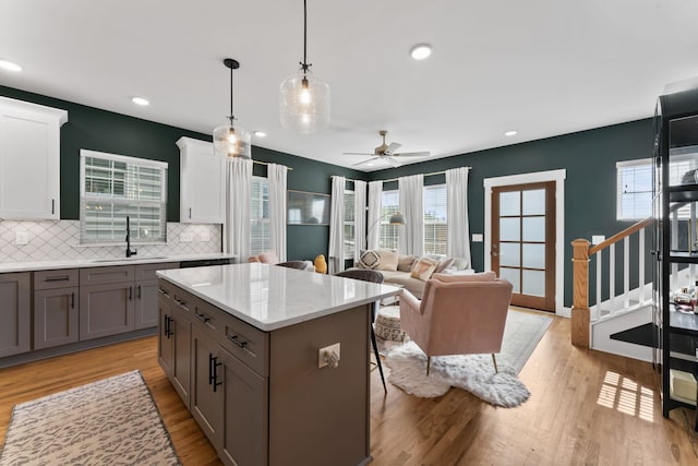 kitchen with sink, decorative backsplash, light wood-type flooring, decorative light fixtures, and white cabinetry