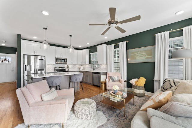 living room featuring ceiling fan, sink, and light wood-type flooring