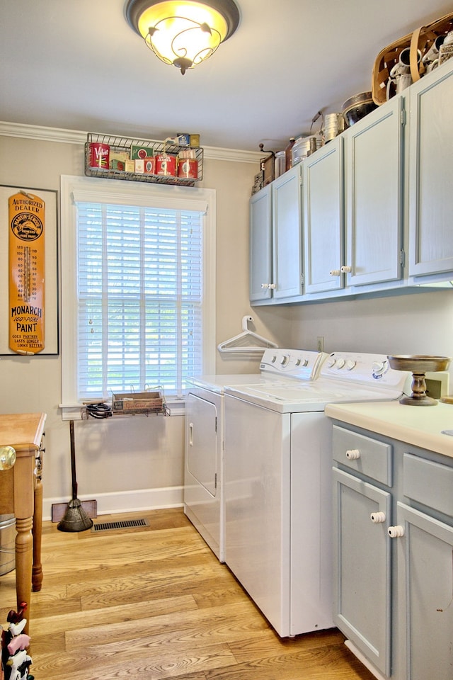 clothes washing area featuring ornamental molding, washing machine and clothes dryer, light hardwood / wood-style floors, and cabinets