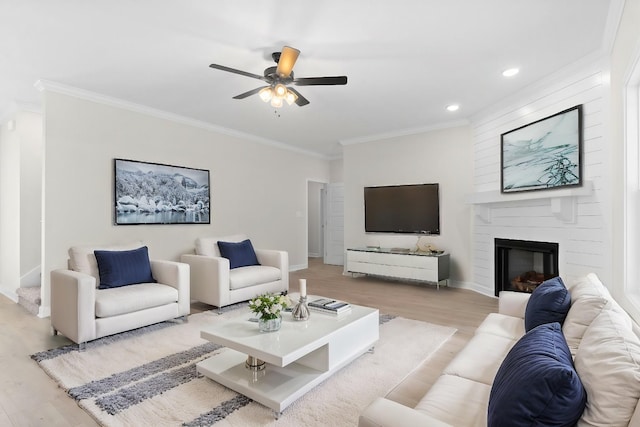 living room featuring ceiling fan, a large fireplace, ornamental molding, and light wood-type flooring