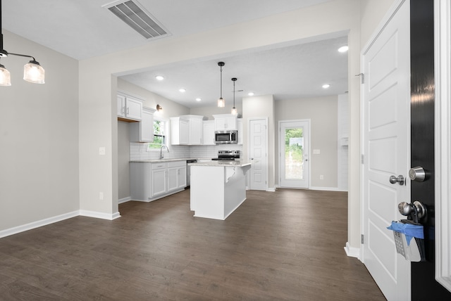 kitchen with white cabinets, appliances with stainless steel finishes, decorative light fixtures, a kitchen island, and dark hardwood / wood-style flooring