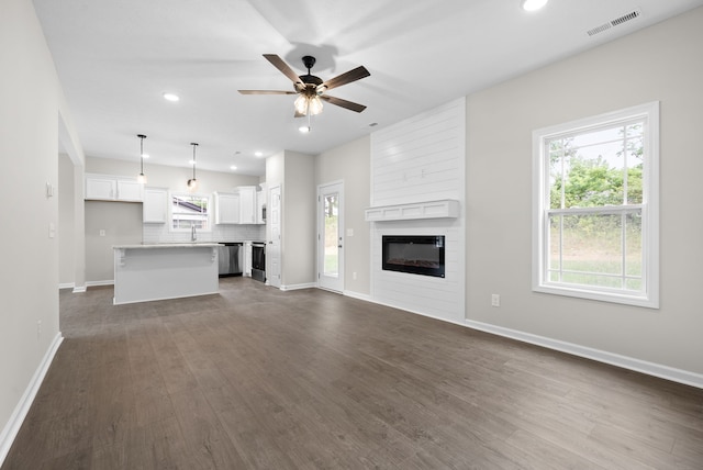 unfurnished living room featuring plenty of natural light, a large fireplace, and dark hardwood / wood-style flooring