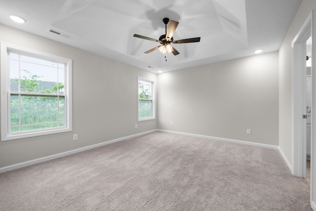 carpeted spare room featuring ceiling fan, a raised ceiling, and a wealth of natural light