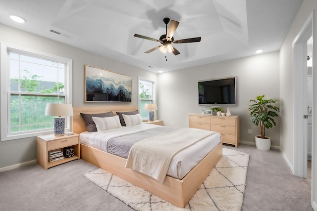 bedroom with light carpet, a tray ceiling, and ceiling fan