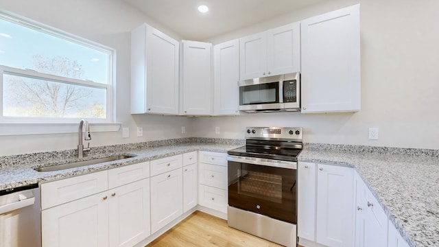 kitchen featuring light hardwood / wood-style flooring, sink, light stone countertops, white cabinetry, and appliances with stainless steel finishes