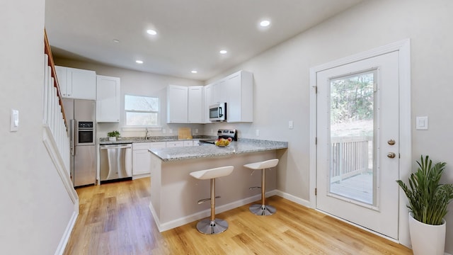 kitchen with plenty of natural light, stainless steel appliances, kitchen peninsula, and white cabinets