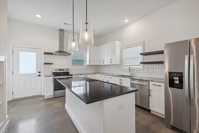 kitchen with wall chimney range hood, appliances with stainless steel finishes, a center island, hanging light fixtures, and white cabinetry