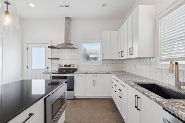 kitchen featuring a healthy amount of sunlight, appliances with stainless steel finishes, white cabinetry, wall chimney exhaust hood, and sink