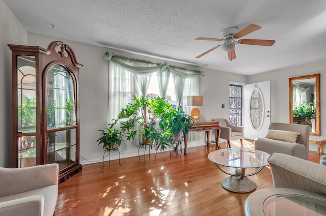 living room with a textured ceiling, light wood-type flooring, a healthy amount of sunlight, and ceiling fan