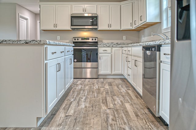 kitchen featuring light stone countertops, appliances with stainless steel finishes, light wood-type flooring, and white cabinetry