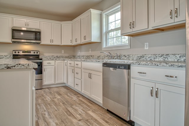 kitchen with appliances with stainless steel finishes, sink, light wood-type flooring, and white cabinets