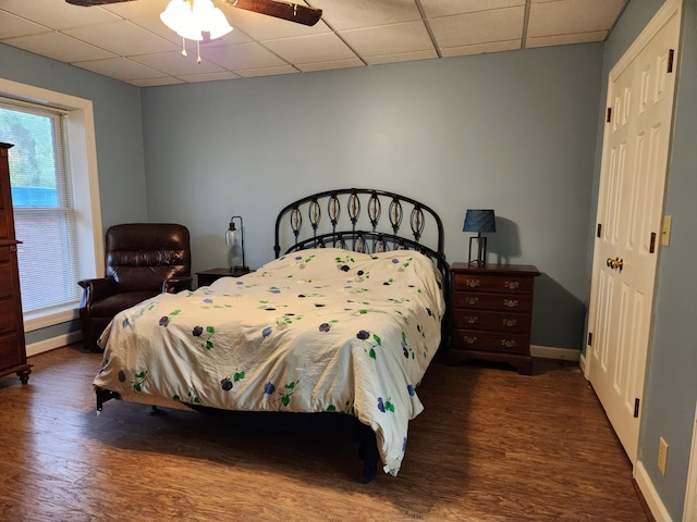 bedroom with dark hardwood / wood-style flooring, a drop ceiling, and ceiling fan