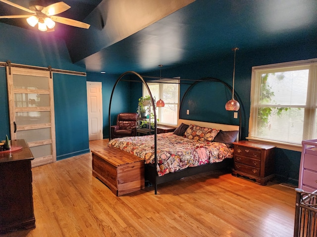 bedroom with multiple windows, a barn door, ceiling fan, and light hardwood / wood-style flooring