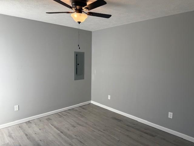 empty room with a textured ceiling, electric panel, ceiling fan, and dark hardwood / wood-style floors