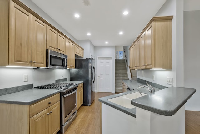 kitchen with stainless steel appliances, kitchen peninsula, sink, light hardwood / wood-style flooring, and light brown cabinetry