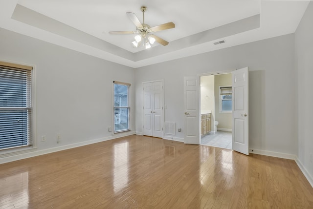 empty room with light hardwood / wood-style floors, ceiling fan, and a tray ceiling