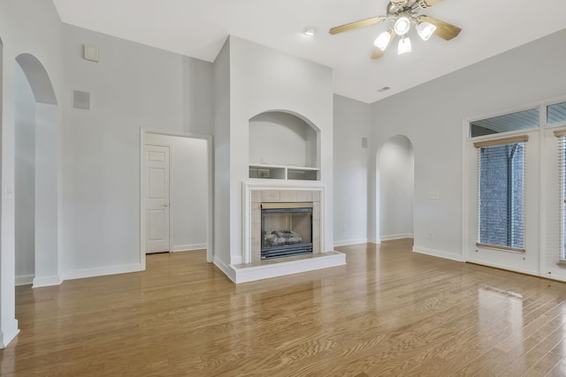 unfurnished living room with ceiling fan, a tile fireplace, light hardwood / wood-style flooring, and built in shelves