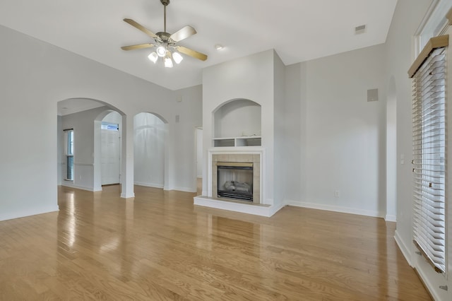 unfurnished living room featuring built in features, a fireplace, ceiling fan, and light hardwood / wood-style flooring