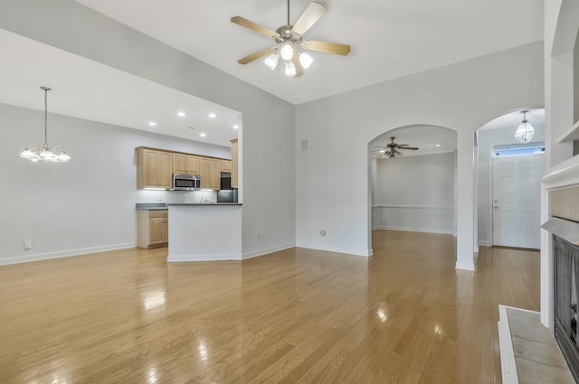 unfurnished living room with ceiling fan with notable chandelier and light hardwood / wood-style flooring