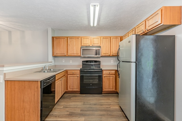 kitchen featuring light hardwood / wood-style flooring, sink, black appliances, light brown cabinetry, and a textured ceiling