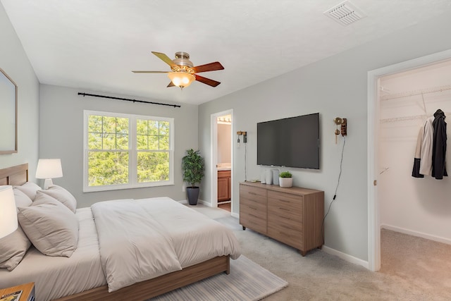 bedroom featuring light carpet, a spacious closet, ensuite bathroom, and ceiling fan