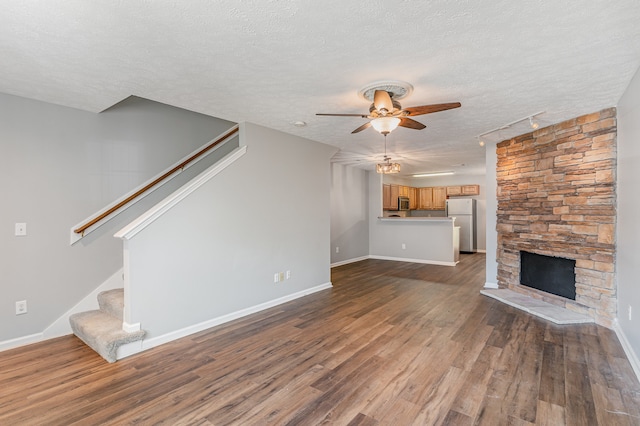 unfurnished living room with a stone fireplace, a textured ceiling, wood-type flooring, and ceiling fan