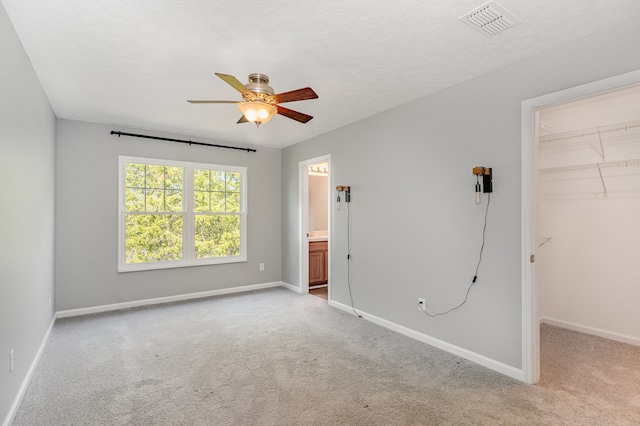 unfurnished bedroom with light colored carpet, a walk in closet, a closet, and ceiling fan