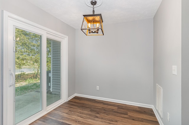 unfurnished dining area with dark wood-type flooring, a textured ceiling, and a chandelier