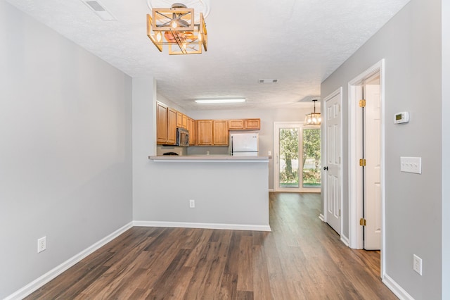 kitchen with a textured ceiling, decorative light fixtures, white refrigerator, and dark hardwood / wood-style floors