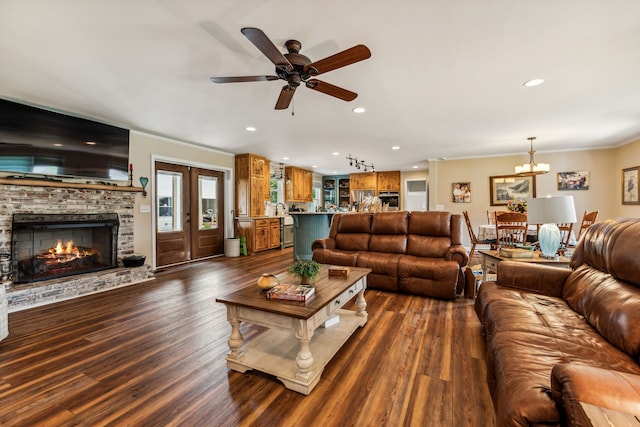 living room featuring dark wood-type flooring, ornamental molding, a fireplace, and ceiling fan with notable chandelier