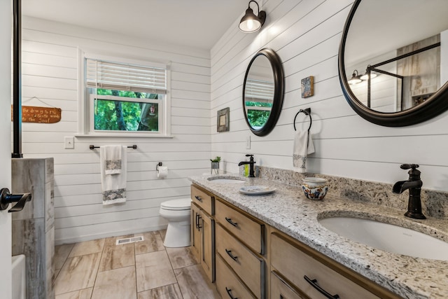 bathroom with vanity, wooden walls, toilet, and a shower with door