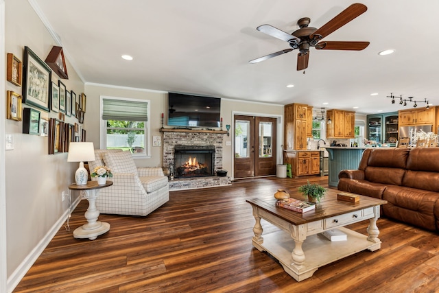 living room with a stone fireplace, ornamental molding, wood-type flooring, and ceiling fan