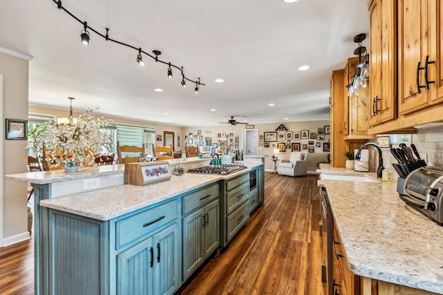 kitchen with dark wood-type flooring, a large island, sink, stainless steel gas stovetop, and light stone counters