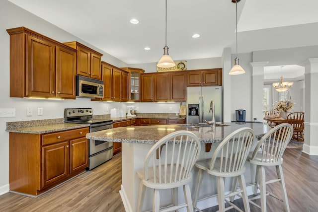 kitchen with light stone counters, stainless steel appliances, hanging light fixtures, and light wood-type flooring