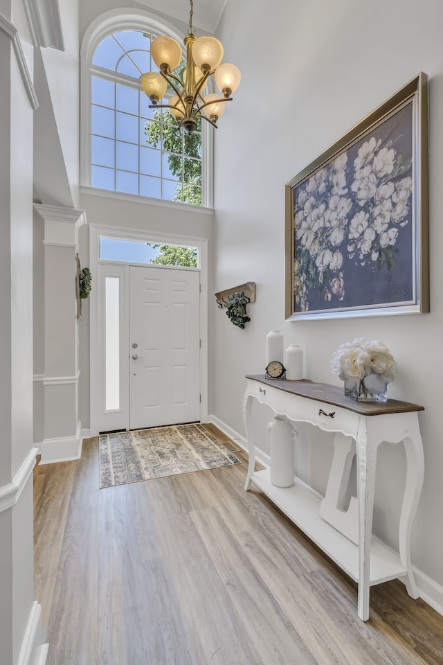 entryway with a notable chandelier, a towering ceiling, and light hardwood / wood-style flooring